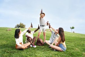 Group of happy people cheering with a beer at music festival. Five friends celebrating outdoors